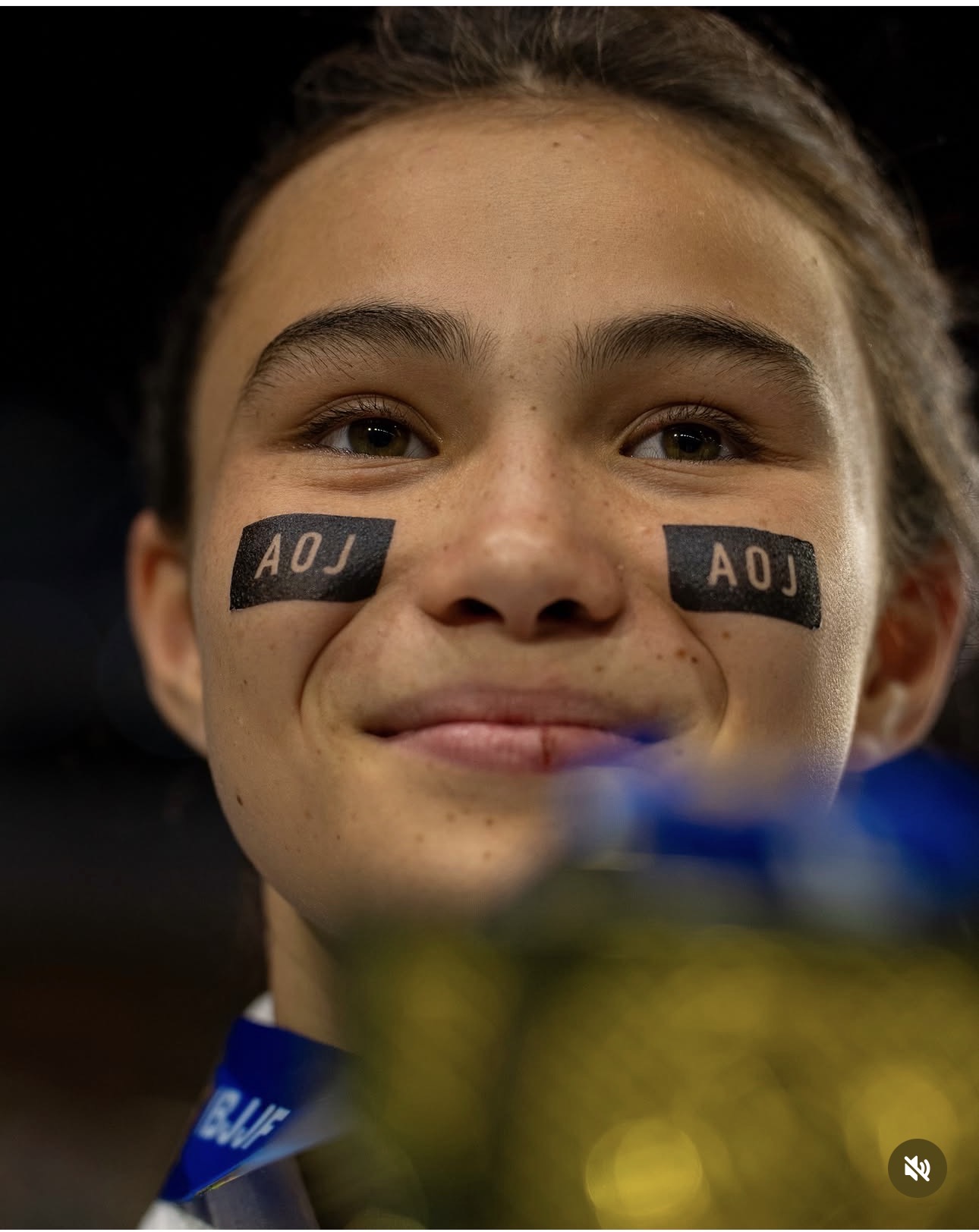Close portrait of Bailey Heinsohn wearing AOJ face tape with a medal blurred in the foreground.